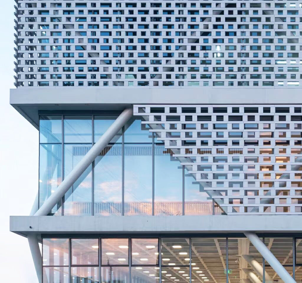 A close-up shot of the dealership's facade, featuring the pristine white LOPO ceramic bricks, highlighting the intricate perforation design and smooth texture of the building's exterior.